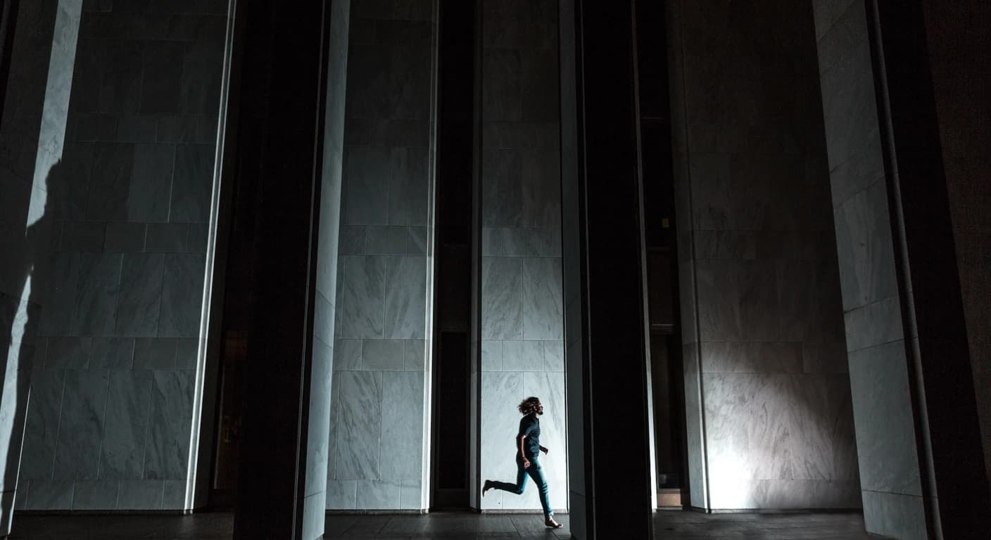 Persona corriendo sola por un corredor oscuro atravesado por haces de luz