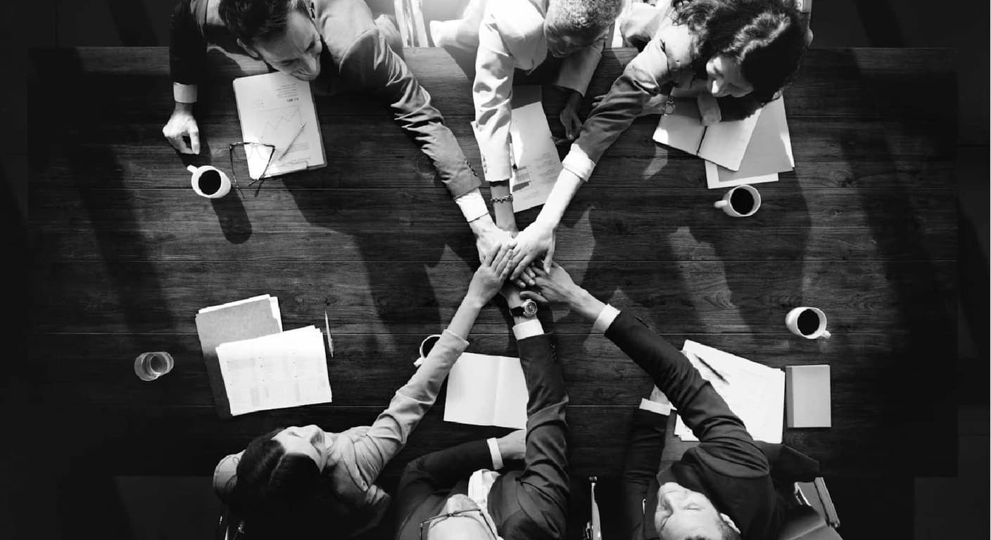 Vista cenital en blanco y negro de un equipo juntando las manos sobre una mesa